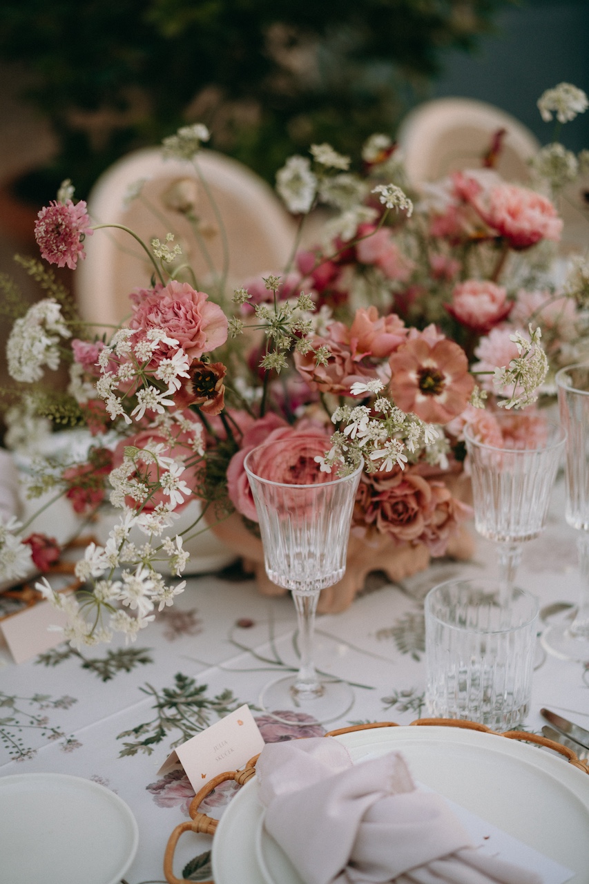 dettaglio mise en place con sottopiatto in bambù e tovaglia con stampa botanica dai toni desaturati per cena di matrimonio all'aperto