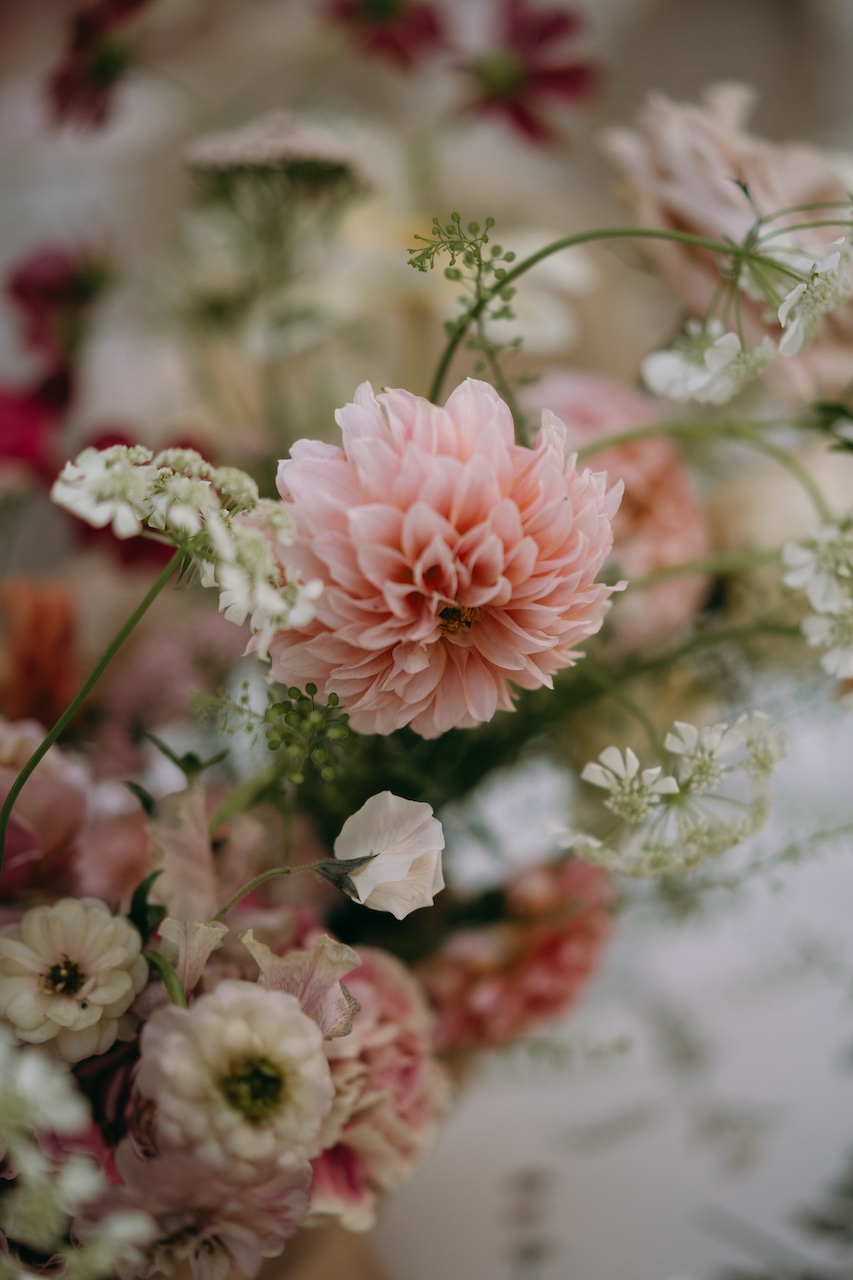 dettaglio centrotavola floreale dai colori desaturati con dalie per cena di matrimonio all'aperto